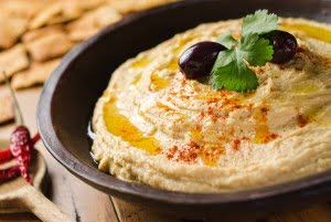 A bowl of creamy hummus with olive oil and pita chips.